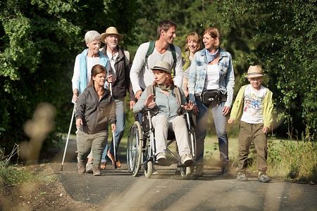 Eine Gruppe Menschen verschiedenen Alters mit und ohne Behinderung wandern durch einen Wald