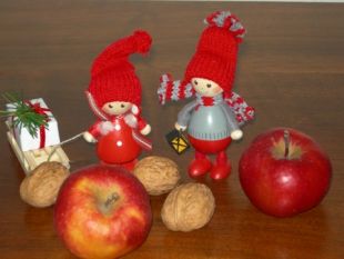Foto: zwei kleine rote Wichtel mit einem Schlitten voller Geschenke stehen zwischen roten Äpfeln und Nüssen