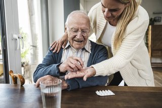 Frau gibt ihrem alten Vater seine Tabletten zur Einnahme.