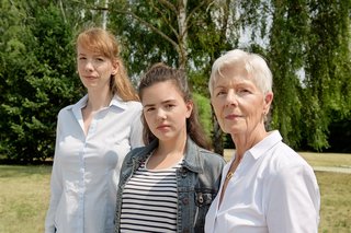 Drei Frauen blicken gemeinsam ernst in die Kamera: Eine jüngere, eine Teenagerin und eine ältere Frau.