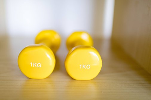 Rehabilitation mit Sport Zwei gelbe Ein-Kilo-Hanteln liegen auf einem Holzboden