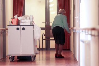 Bewohnerin einer Senioren-Residenz, sie geht über den Gang in ein Zimmer