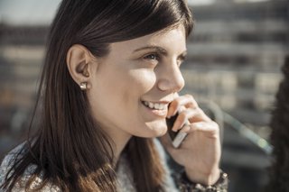 Eine junge Frau telefoniert lächelt, sie trägt ein Hörgerät im rechten Ohr