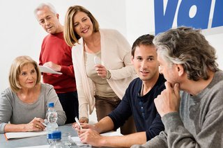 Verschiedene Menschen sitzen an einem Tisch, offenbar in einer Arbeitssitzung, an der Wand hinter ihnen ist ein großes VdK-Logo.