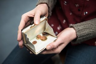 Hände einer Frau halten eine Geldbörse offen, darin befinden sich wenige Münzen. 