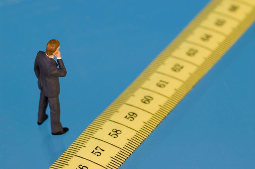 Renteneintrittsalter Ein Figürchen steht vor einem Maßband, auf dem die Zahlen ab 57 aufwärts zu sehen sind, als Symbol für das Renteneintrittsalter