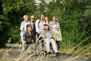 Eine Gruppe unterschiedlicher Menschen - mit und ohne Behinderung, alt und jung, Männer und Frauen - wandern gemeinsam im Grünen. 