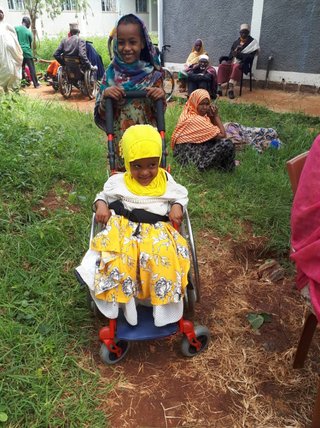 Zwei äthiopische kleine Mädchen, eins schiebt das andere im Reha-Buggy