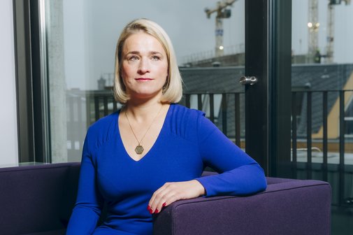 Verena Bentele Verena Bentele sitzt auf einem Sofa, hinter ihr sieht man die Silhouette von Berlin.