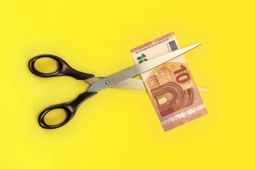 Schere Armut Reichtum - Soziale Spaltung Eine Schere zerschneidet vor gelbem Hintergrund einen 10-Euro-Schein