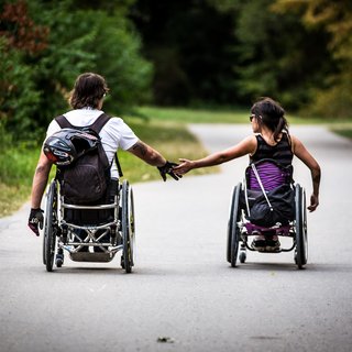 Ein junger Mann und eine junge Frau im Rollstuhl, sie fahren nebeneinander, halten sich an der Hand. Das Foto zeigt Lisa Schmidt und David Lebuser; beide sind Wheelchairskater und testen den Skatepark in München.