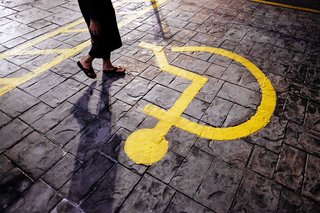 Eine Frau geht über einen gepflasterten Bereich mit einem gelben Piktogramm für einen Behindertenparkplatz.