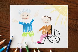 Eine bunte Kinderzeichnung zeigt eine Person, die im Rollstuhl sitzt und eine Person, die im Stehen jubelnd die Arme nach oben streckt. Neben dem Bild liegen Buntstifte.
