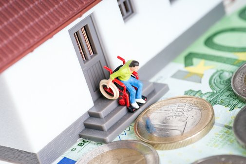 Barrierefrei umbauen Ein Spielzeughaus, auf der Türschwelle sind Stufen. Ein Figürchen im Rollstuhl steht an der Schwelle, schaut nach unten. Vor dem Spielzeughaus liegen Geldscheine und -münzen.
