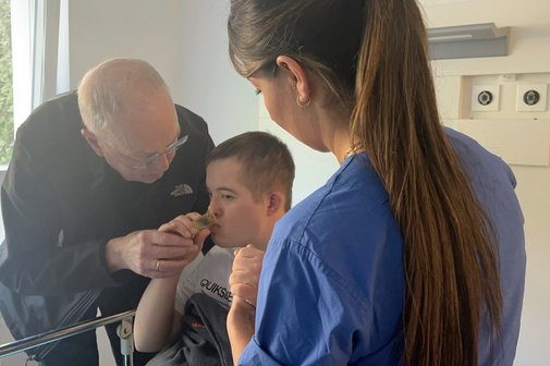 Inklusive Medizin Klinik Hagen-Haspe Ein Junge mit Down-Syndrom wird von einer jungen Frau im Arztkittel untersucht, der Vater steht neben dem Kind und beruhigt es.