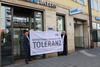 Auf dem Foto sieht man die Landesgeschäftsführung, Michael Pausder (rechts) und Marian Indlekofer, die ein ein Bündnis-Banner vor der VdK-Landesgeschäftsstelle in München präsentieren.