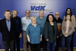 Neun Frauen und Männer stehen vor einem blauen Hintergrund mit VdK-Logo.