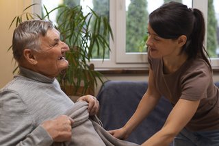 Eine junge Frau legt einem Mann im Rollstuhl eine Decke über die Beine.