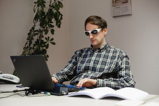 Ein Mann arbeitet mit einer verdunkelten Sehhilfe an seinem LapTop.