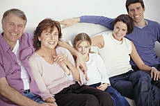 Symbolfoto: Eine Familie, bestehend aus Großeltern, Eltern und Enkelin, gemeinsam auf einer Couch