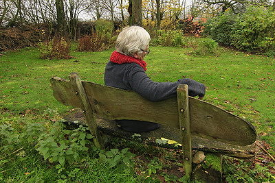 Foto:ältere Frau sitzt alleine auf einer Parkbank