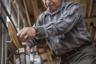 Ein älterer Mann bearbeitet Holz an einer Maschine.