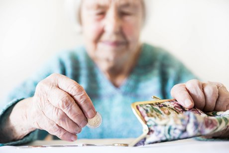 Eine Seniorin sitzt an einem Tisch, zählt Münzen in ihr Portemonaine. Ihr Gesichtsausdruck ist ernst.