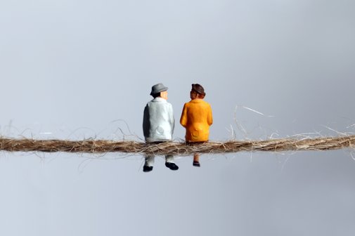 Leben im Alter Zwei Mini-Figürchen eines älteren Mannes und einer älteren Frau sitzen nebeneinander auf einem dünnen Seil mit dem Rücken zum Betrachter