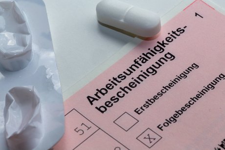 Eine Arbeitsunfähigkeitsbescheinigung, auf der "Folgebescheinigung" angekreuzt ist, und Tabletten