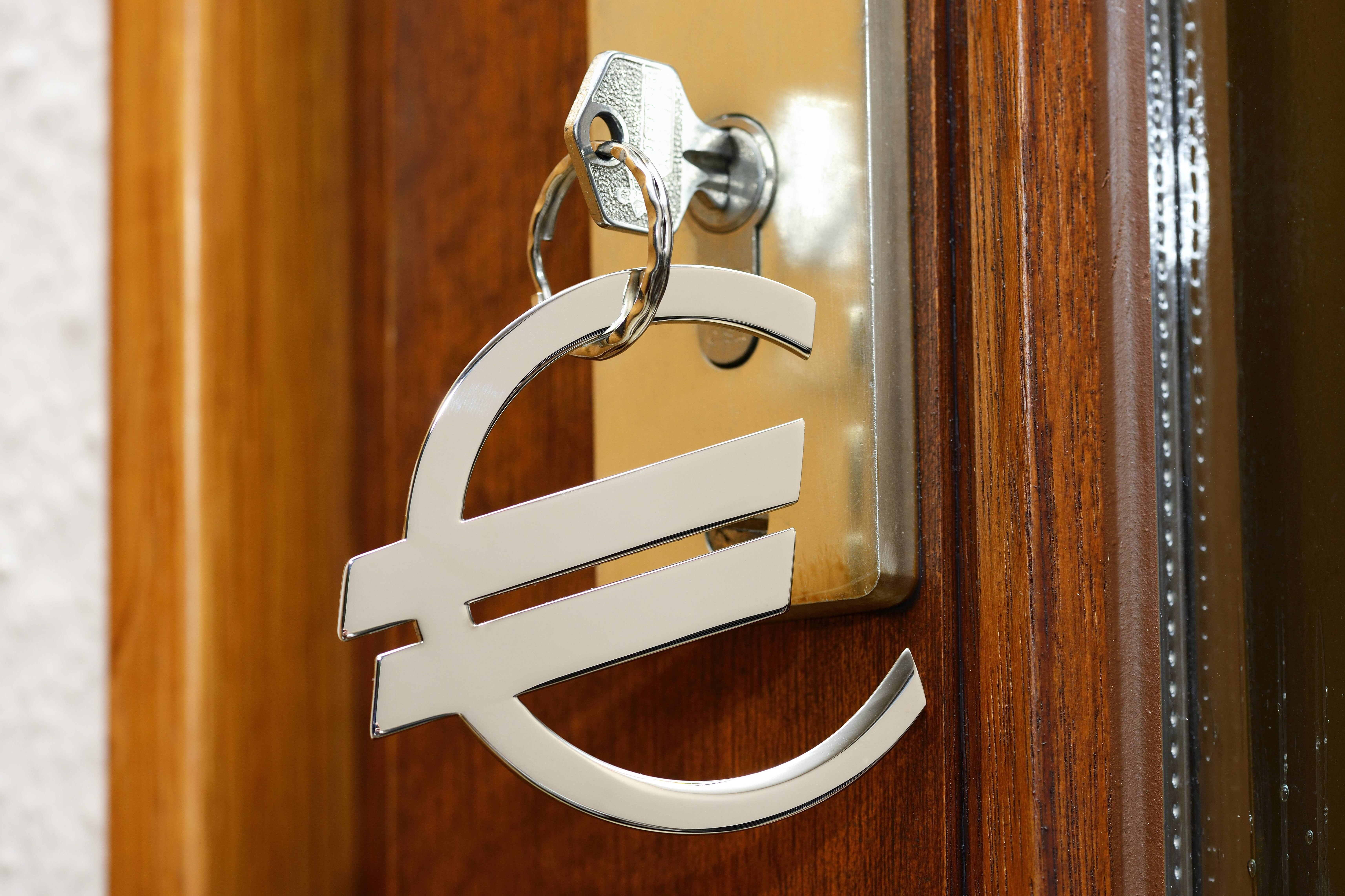 Ein Schlüssel steckt im Türschloss einer Wohnungstür, der Schlüsselanhänger ist ein großes Euro-Zeichen. 