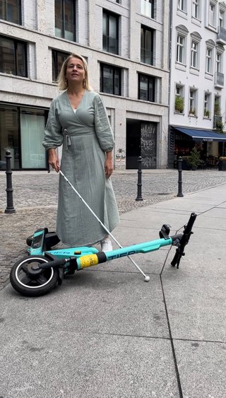 VdK-Präsidentin Verena Bentele steht mit ihrem Blindenlangstock auf einem Platz, vor ihr liegt ein umgekippter E-Scooter