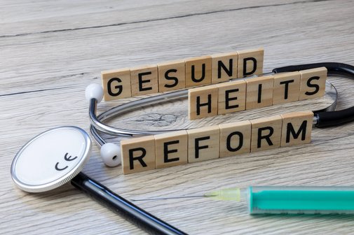 Gesundheitsreform Holzbuchstaben bilden das Wort "Gesundheitsreform". Daneben liegt ein Stethoskop.