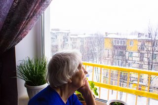 Ältere Frau sitzt am Fenster und schaut in den fallenden Schnee