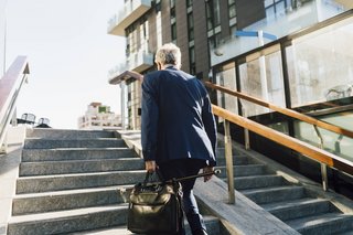 Ein älterer Mann im Business-Anzug und mit Aktentasche läuft eine Treppe hinaus, man sieht ihn von hinten