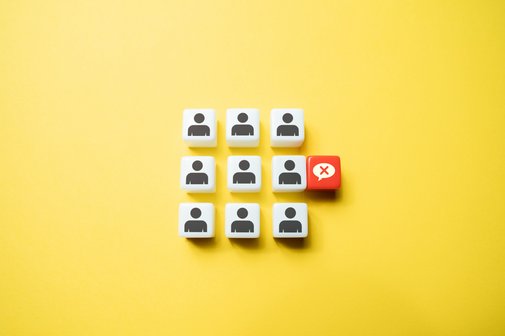 Diskriminierung am Arbeitsplatz Symbolbild für Diskriminierung am Arbeitsplatz: Neun Würfel mit einem Personen-Icon sind in einem 3x3-Raster auf gelbem Hintergrund. Neben einer der Figürchen ist eine durchgestrichene Sprechblase.