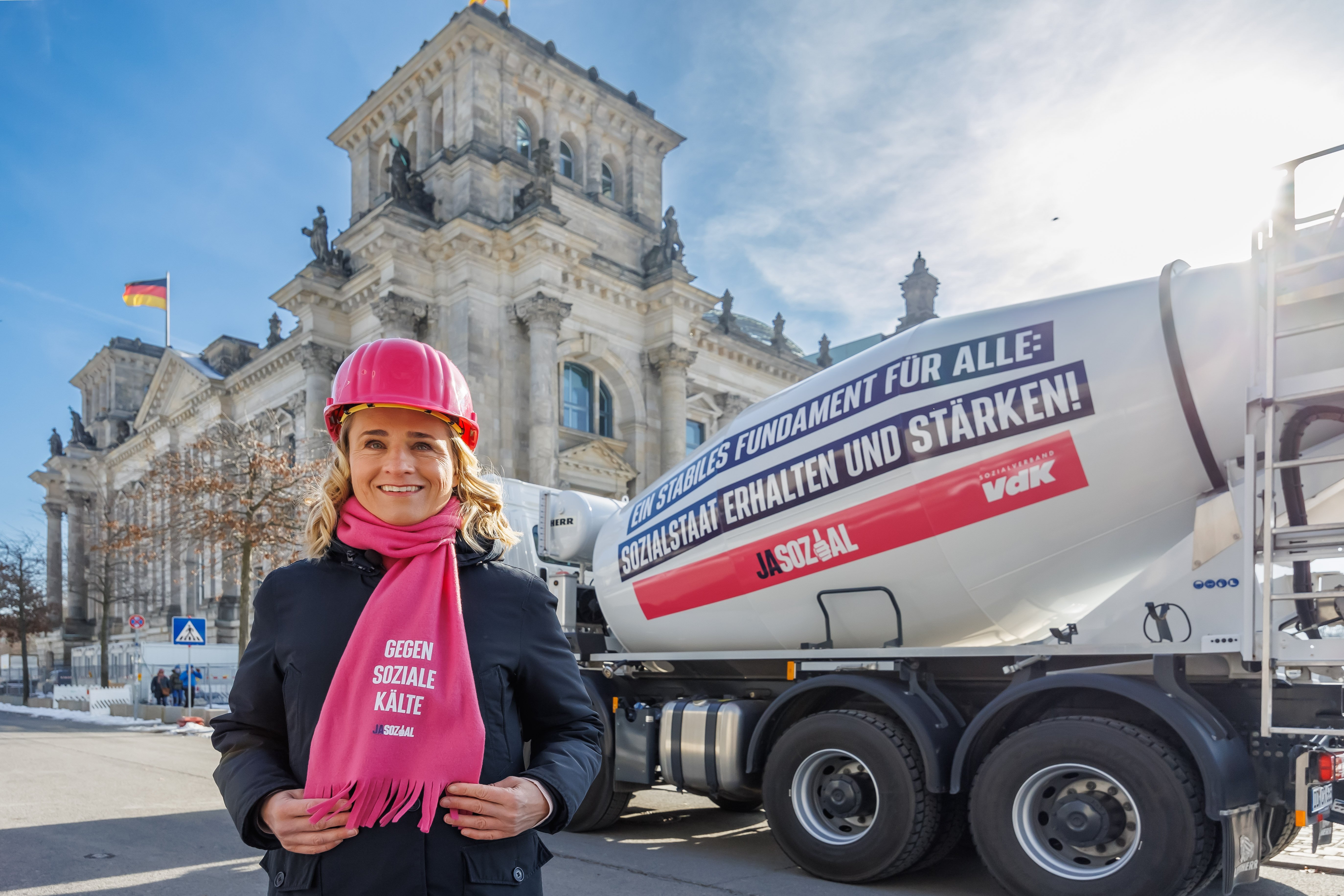 VdK-Präsidentin Verena Bentele vor dem Bundestag; sie steht neben einem riesigen Betonmischer mit der Aufschrift "Ein starkes Fundament für alle: Sozialstaat erhalten und stärken!" und den Logos JASOZIAL und Sozialverband VdK Deutschland 