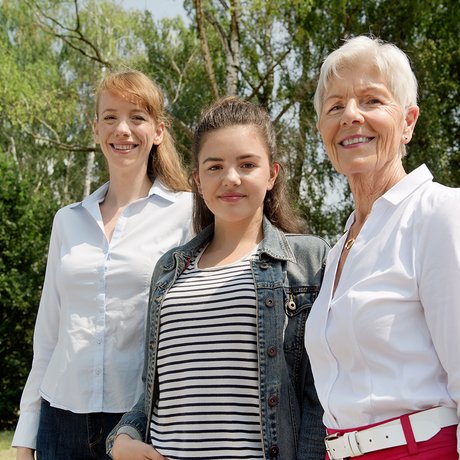 Drei Frauen lächeln gemeinsam in die Kamera: Eine jüngere, eine Teenagerin und eine ältere Frau.