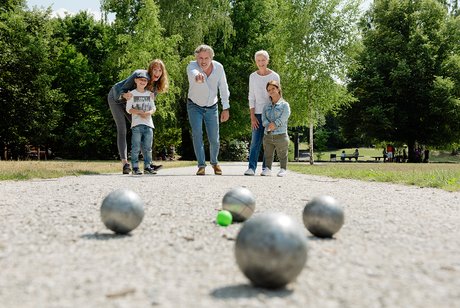 KInder und Erwachsene auf einer Boule-Bahn beim gemeinsamen Spiel. 