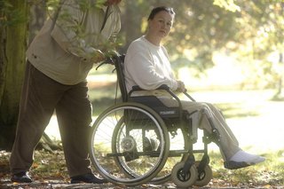 Mann schiebt Frau im Rollstuhl durch den Park