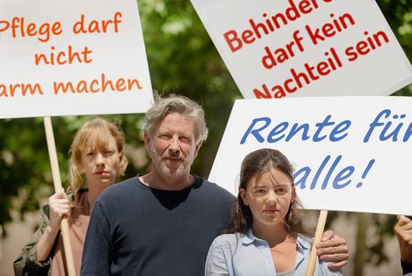 Gruppe von Menschen verschiedenen Geschlechts und Alters, mit und ohne Behinderung, demonstrieren. Auf den Demopappen steht "Pflege darf nicht arm machen", "Behinderung darf kein Nachteil sein" und "Rente für alle"