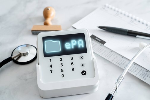 elektronische Patientenakte Ein Kartenlesegerät, auf dessen Display "ePA" steht. Außerdem liegen auf dem Tisch ein Stethoskop, ein Kalender mit Kugelschreibe und ein Stempel.