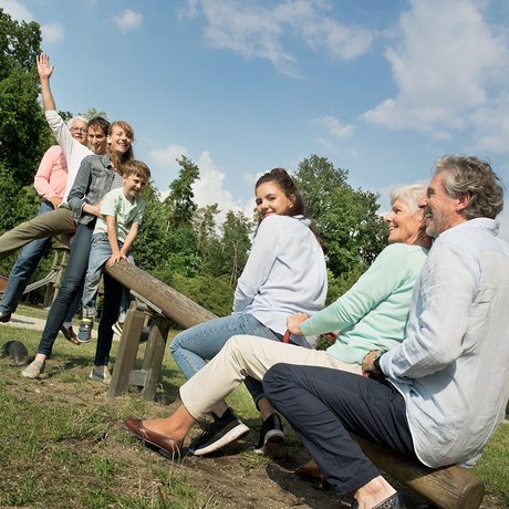 Junge und alte Menschen und ein Kind sitzen auf einer Wippe auf einem Spielplatz