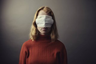Eine junge Frau hat eine Atemschutzmaske über die Augen gezogen, so dass sie nichts sehen kann.