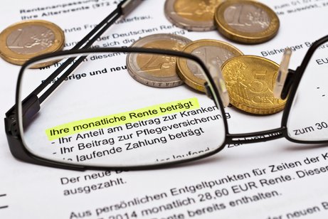 Rentenbescheid Nahaufnahme eines Rentenbescheids mit markiertem Text ‚Ihre monatliche Rente beträgt‘, umgeben von Euro-Münzen und einer Brille im Vordergrund.
