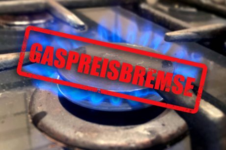 Gasherd im Privathaushalt mit brennender Flamme, darüber ist ein Stempel auf das Foto montiert mit der Aufschrift "Gaspreisbremse"