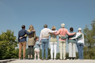 VdK-Mitglieder unterschiedlichen Geschlechts und Alters, mit und ohne Behinderung, stehen mit dem Rücken zum Betrachter Arm in Arm. Eine kleinwüchsige Frau dreht sich um und blickt in die Kamera. 