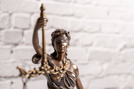 Eine bronzene Statue der Justitia vor einer gemauerten weißen Wand