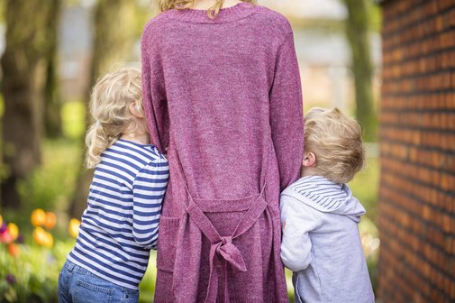 Mutter mit zwei Kindern Rückenansicht einer Mutter, die rechts und links ein kleines Kind an den Händen hält, die Kinder schmiegen sich an sie.