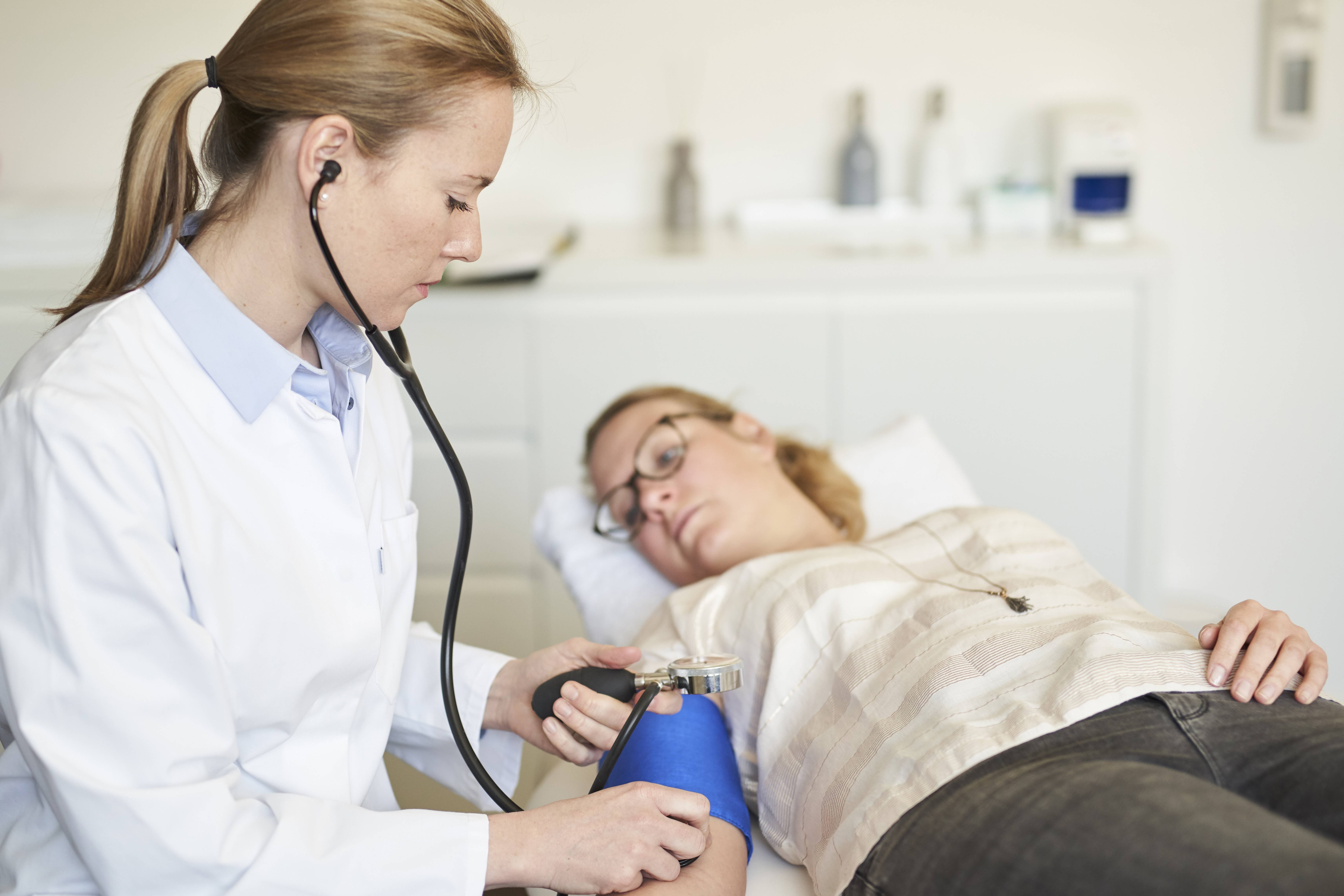 Ärztin misst Blutdruck bei liegender Patientin