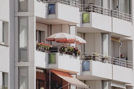 Blick auf Balkone eines Plattenbaus, ein Balkon hat einen roten Sonnenschirm, ein anderer eine Markise